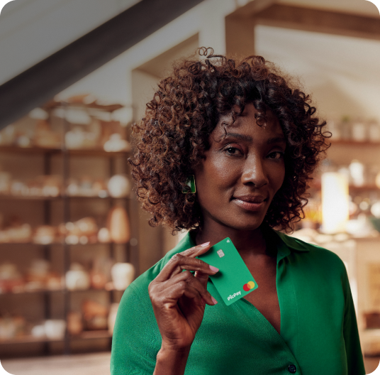 Mulher de blusa verde em uma loja de cerâmica segurando um cartão gold do PicPay.