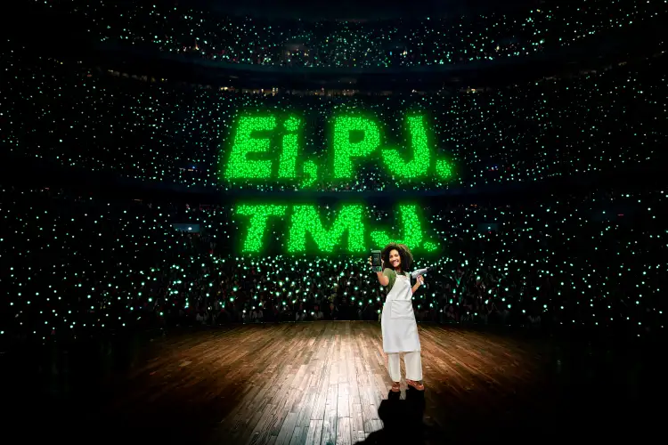 Mulher segurando uma maquininha de cartão PicPay em um palco, diante de uma multidão iluminada em verde.