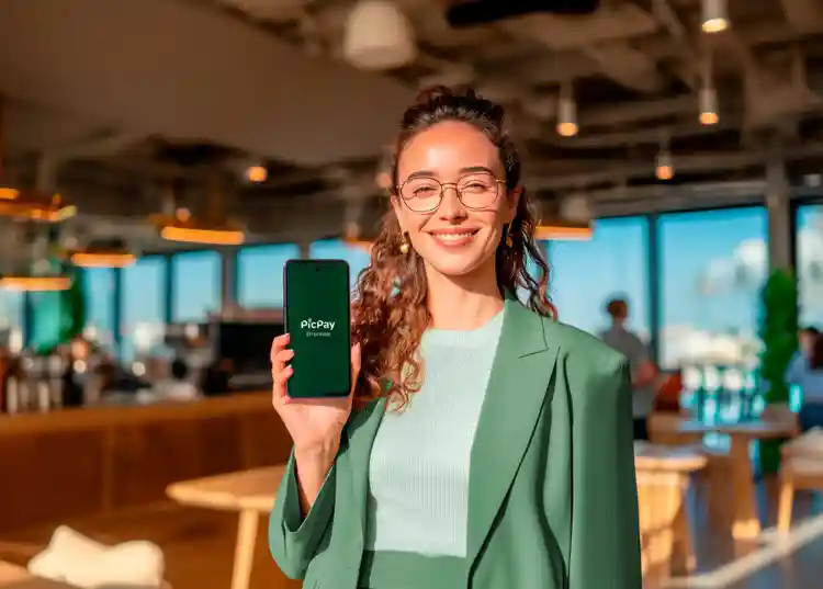 Pessoa em ambiente comercial interno, segurando um celular com o aplicativo PicPay Empresas exibido na tela.